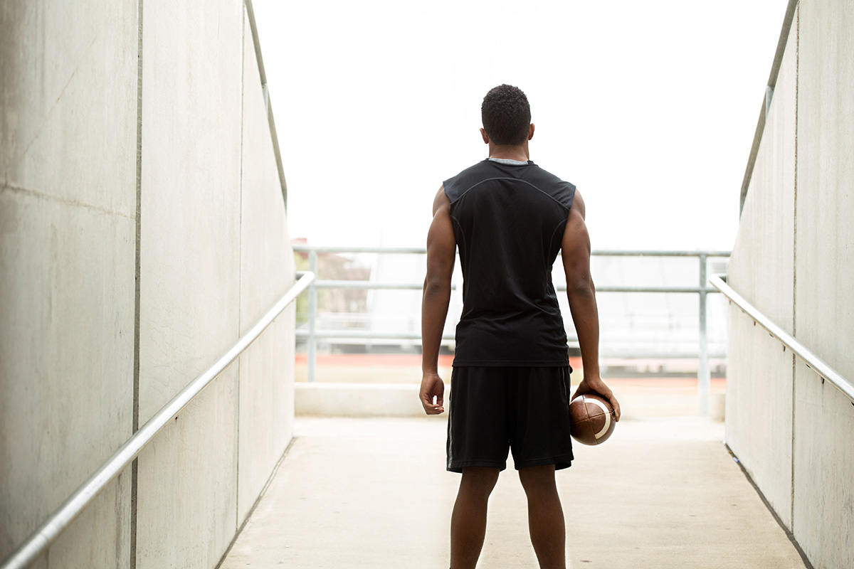Rear view of a teenager holding a football I Want to Learn