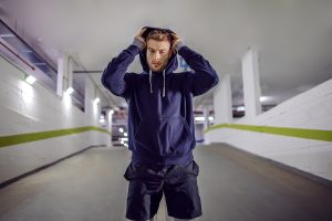 Young sportsman putting hoodie on head while standing in underground garage anxiety in athletes.
